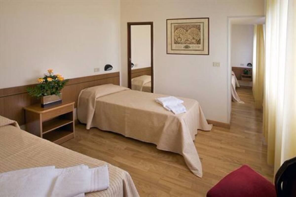 Habitación de hotel con dos camas, piso de madera, mesita de noche con un jarrón de flores, espejo y un cuadro en la pared.