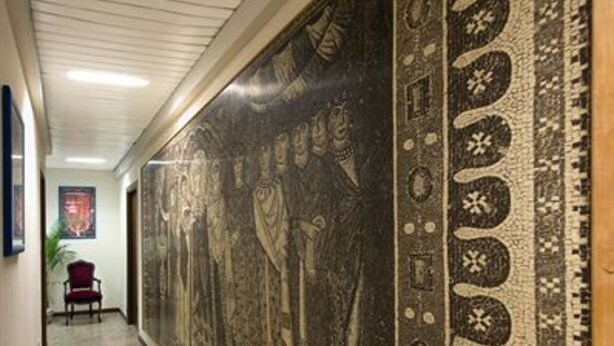 Un couloir orné d’une grande fresque murale à motifs, avec une chaise rouge et un tableau encadré accroché au mur.