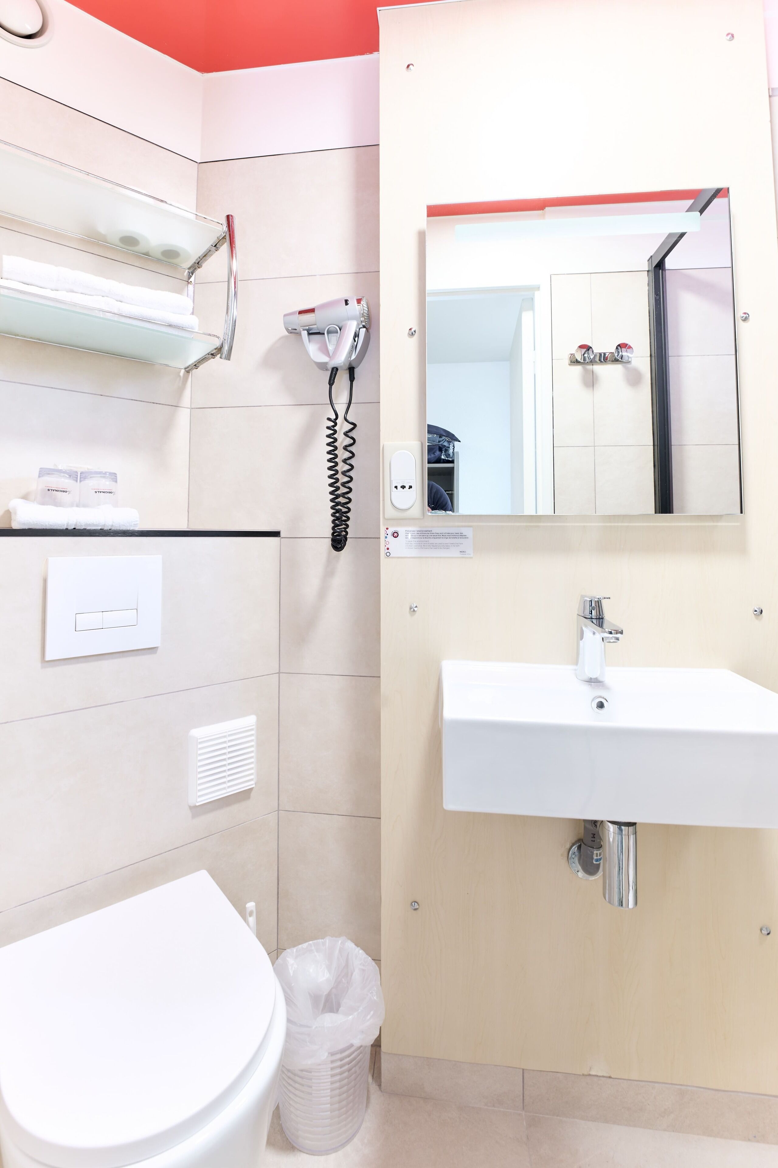 A modern bathroom with a white toilet, a sink, a mirror, and a hairdryer on the wall.