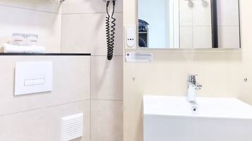 A modern bathroom with a white toilet, a sink, a mirror, and a hairdryer on the wall.