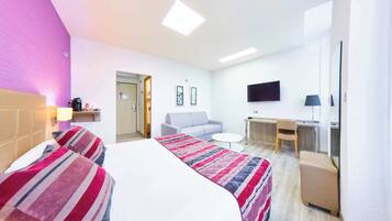 A hotel room with a bed, two bedside tables, a sofa, a desk, a TV, and a chair.