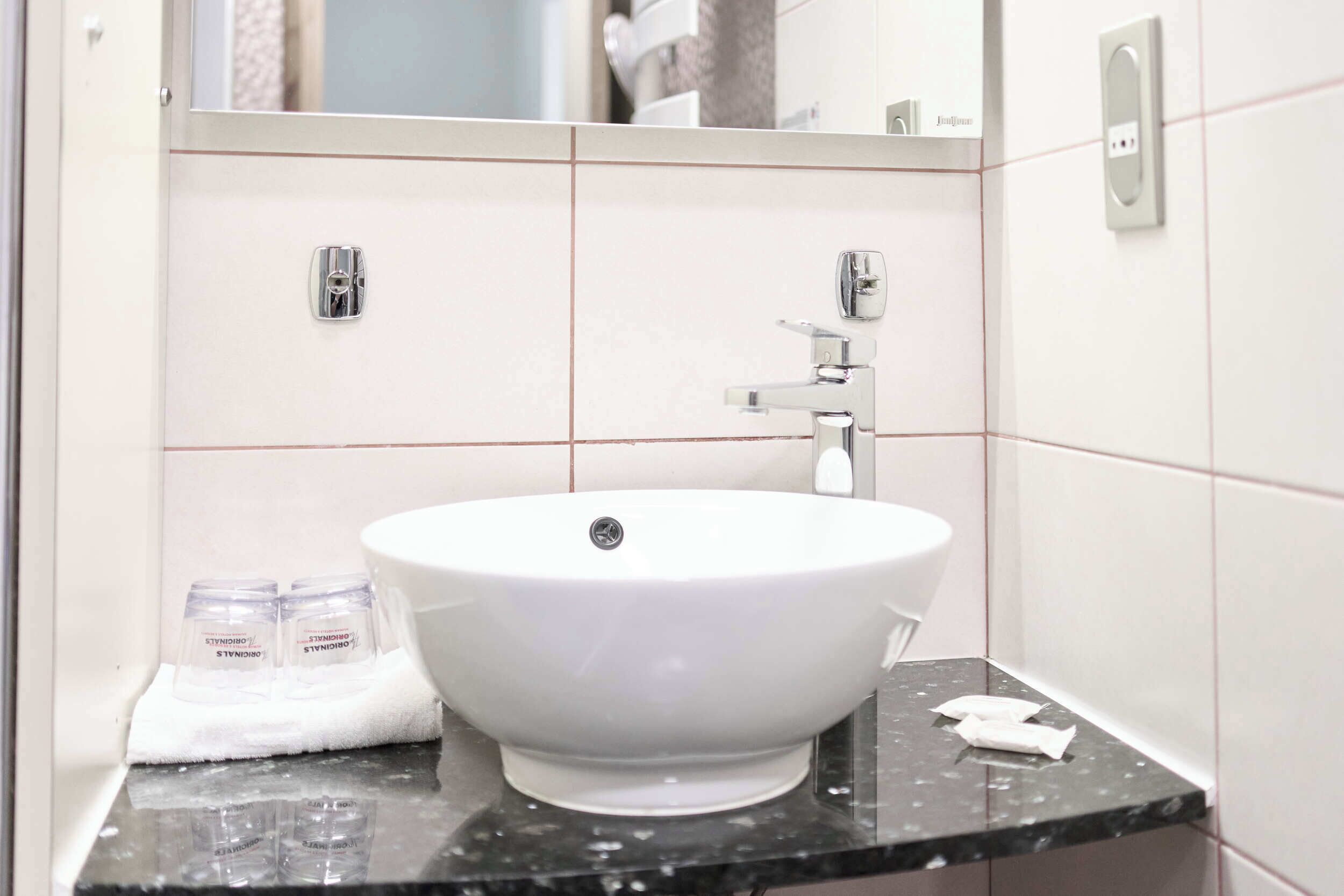 A bathroom with a white sink, two soap dispensers, a towel, and a mirror.