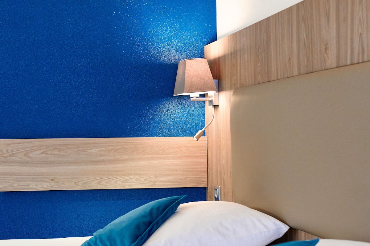 A bed with two pillows, a wooden headboard, and a blue wall.
