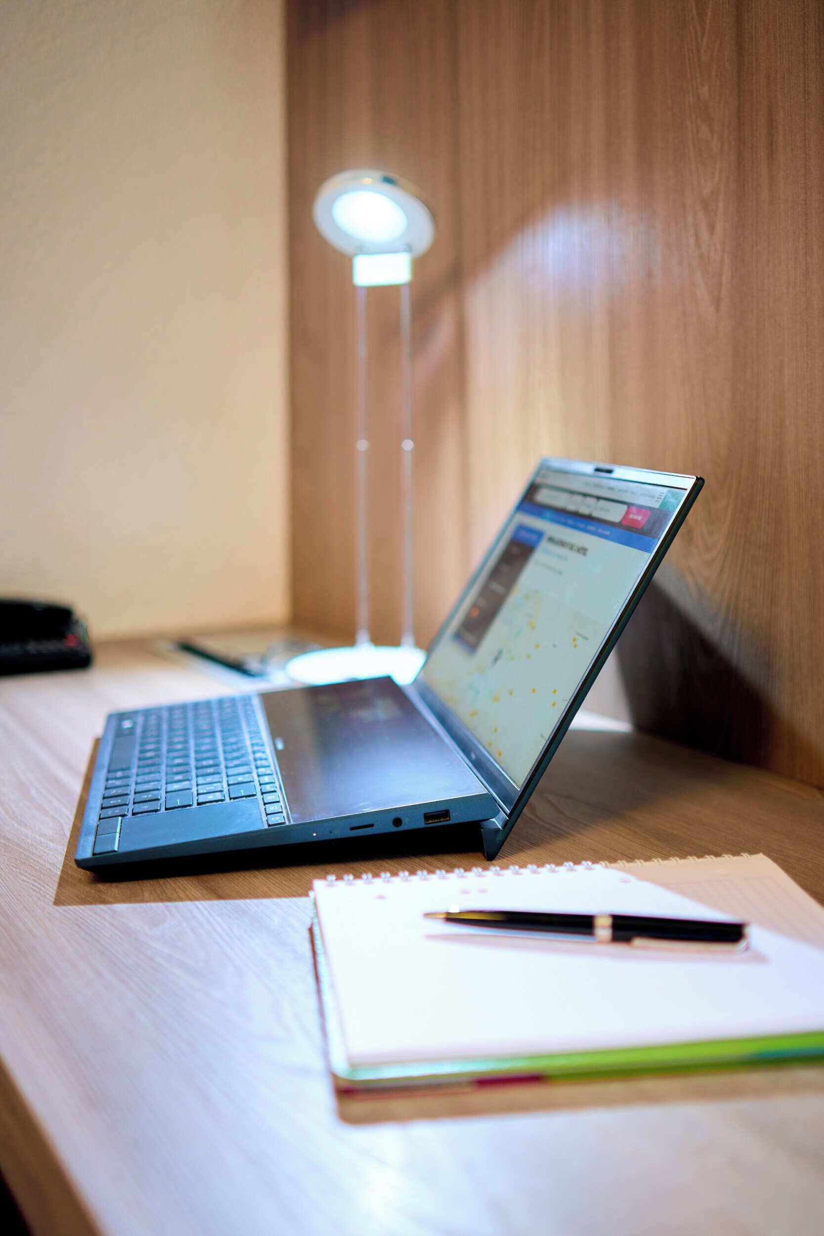 A laptop on a wooden desk with a notebook and pen beside it.