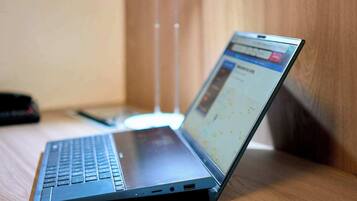A laptop on a wooden desk with a notebook and pen beside it.
