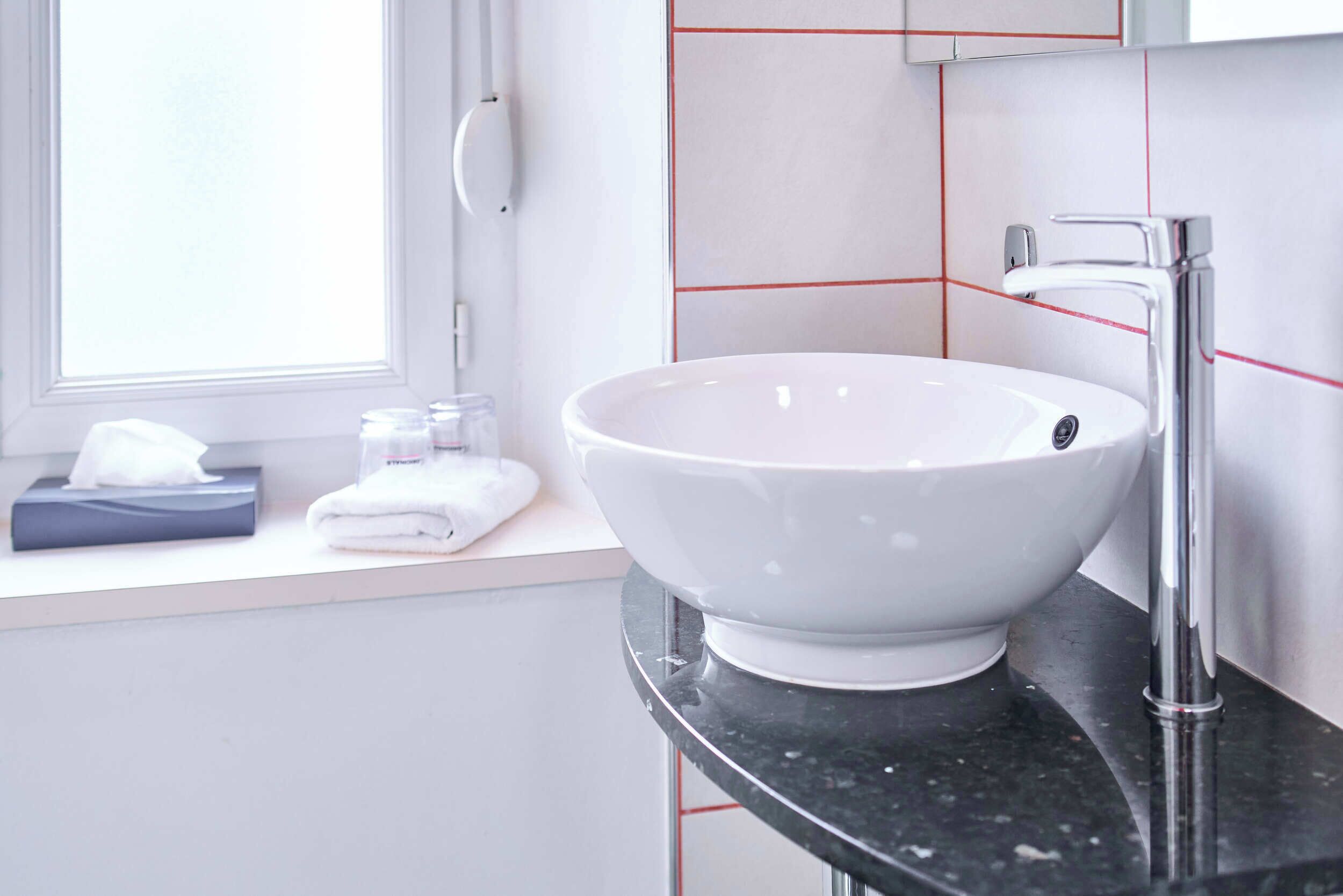 Une salle de bain avec un lavabo blanc, un robinet moderne et une fenêtre.