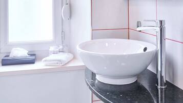 Une salle de bain avec un lavabo blanc, un robinet moderne et une fenêtre.