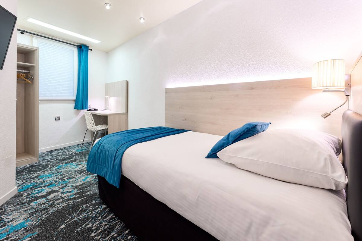 A hotel room with a bed, a desk, a chair, and a wardrobe.