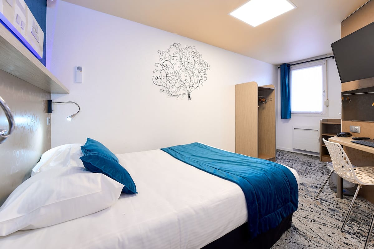 A hotel room with a bed, a desk, a chair, a wardrobe, and a wall decoration.