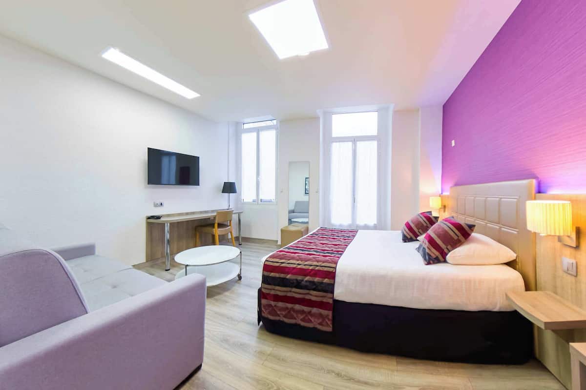 A modern hotel room with a bed, a desk, a chair, a TV, and a window.