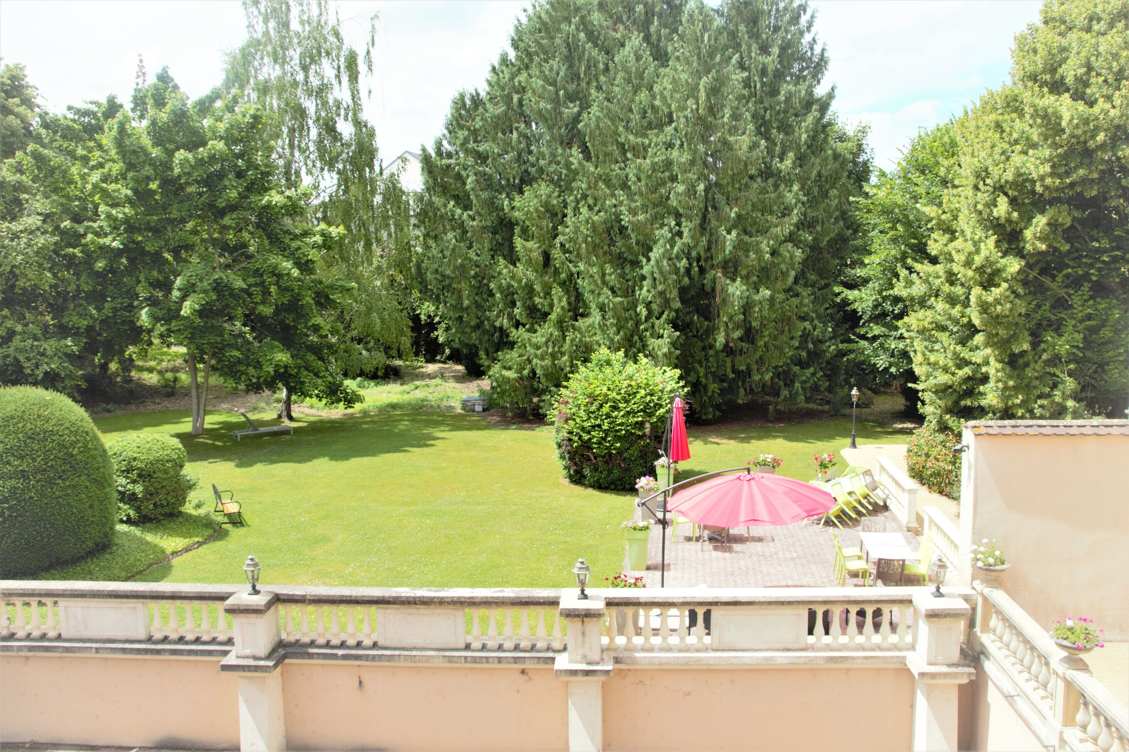A courtyard with a lawn, a red umbrella, and a seating area with chairs and tables.