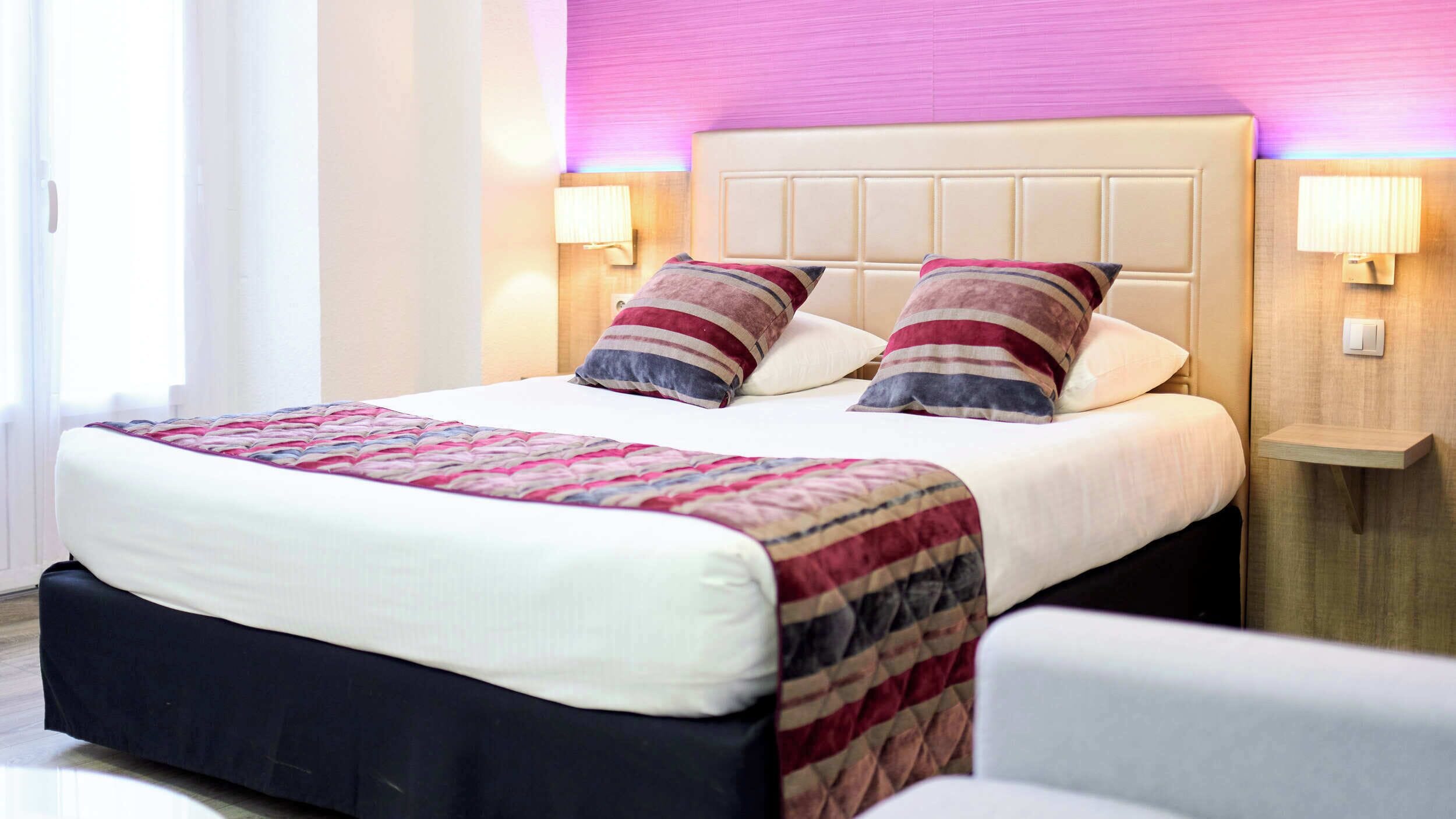 A hotel room with a large bed, two bedside lamps, a headboard, and a bedside table.