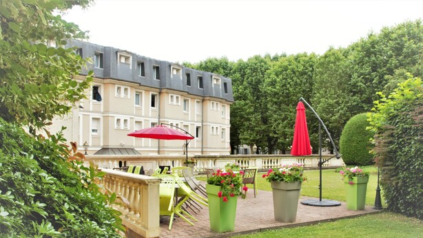 Ein Hotelinnenhof mit Außenbestuhlung, Topfpflanzen und einem roten Sonnenschirm.