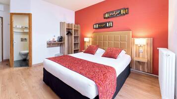 A hotel room with a large bed, wooden headboard, two bedside tables with lamps, a wardrobe, and a small shelf with toiletries.