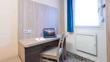 A modern room with a wooden desk, a laptop, a chair, a window with blue curtains, and a wall-mounted air conditioner.