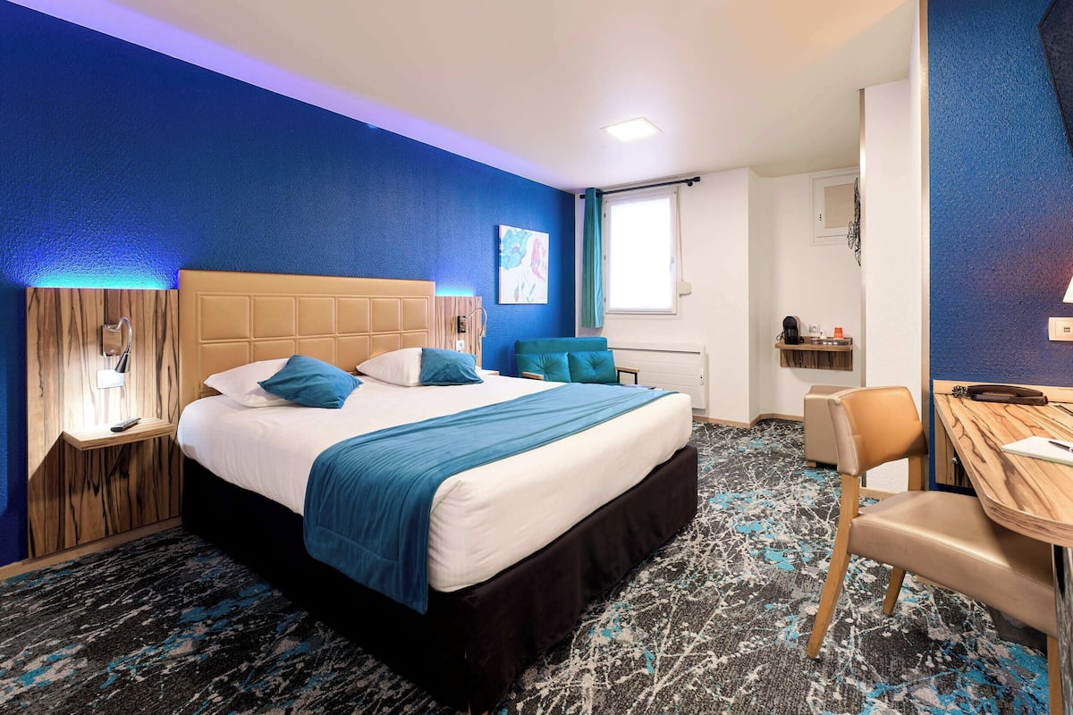 A hotel room with a large bed, a desk, and a chair.