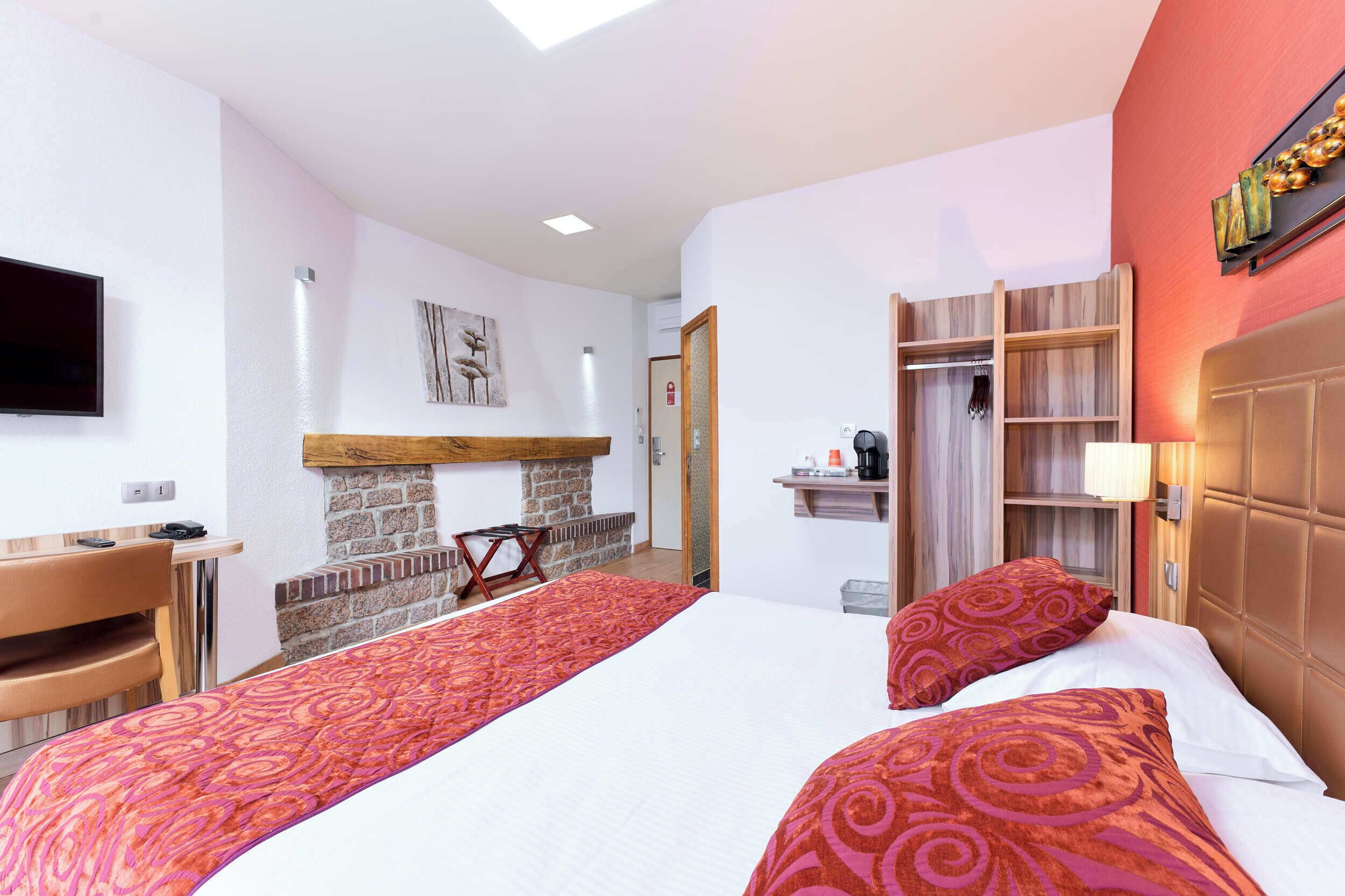 A hotel room with a bed, a desk, a TV, a fireplace, and a wardrobe.