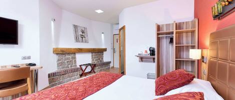 A hotel room with a bed, a desk, a TV, a fireplace, and a wardrobe.