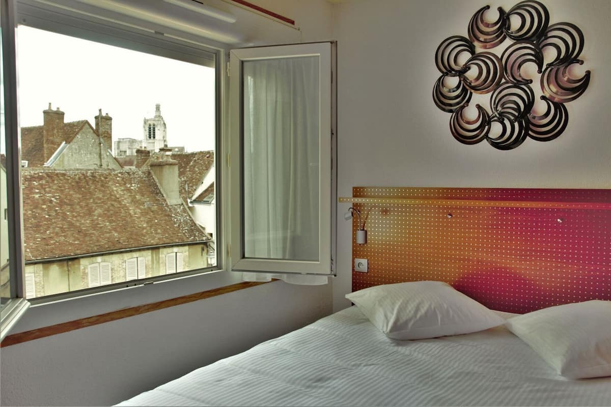 A bedroom with a bed, a window with curtains, and a wall decoration.