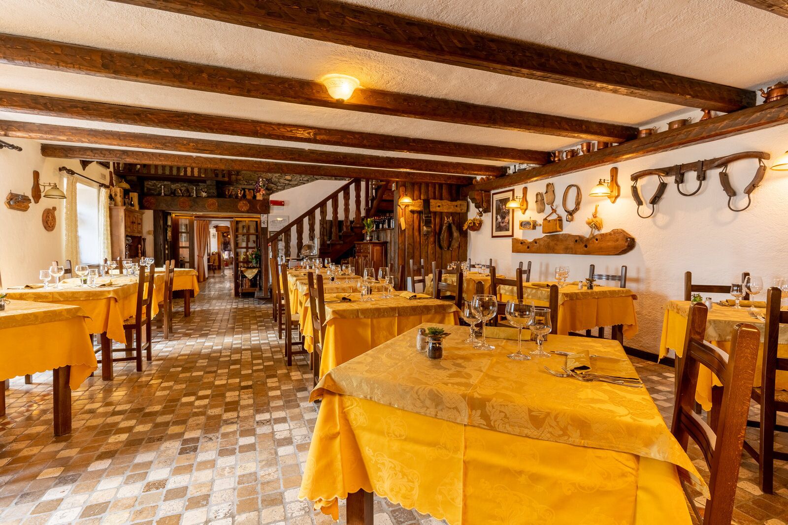 Un restaurant avec de nombreuses tables dressées pour le service, des poutres en bois au plafond et un sol à carreaux.