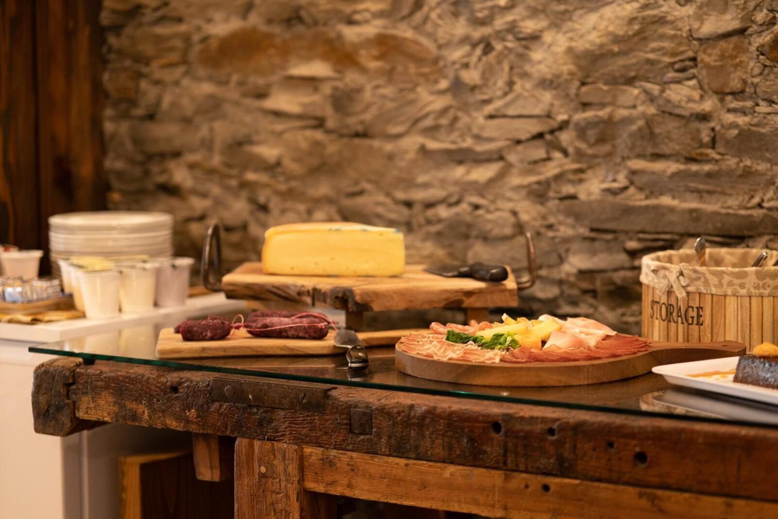 A rustic wooden table with various cheeses, cured meats, and a cheese board.