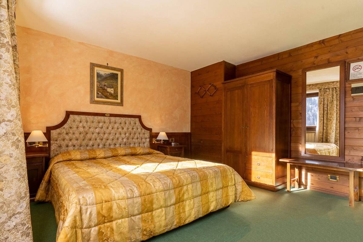 A bedroom with a large bed, wooden wardrobe, and a painting on the wall.
