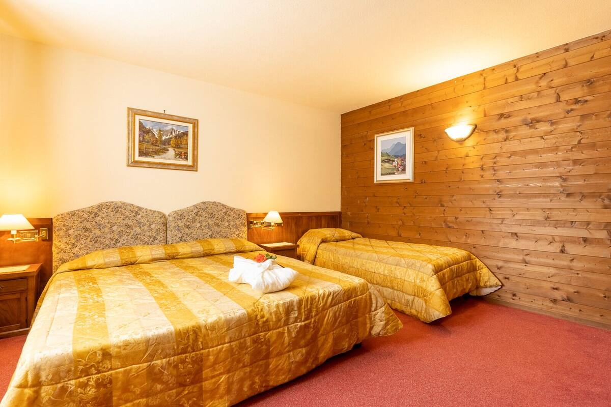 A hotel room with two beds, wooden paneling on one wall, and two framed pictures.