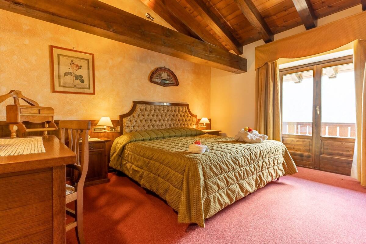 A cozy room with a wooden bed, a desk with a chair, a framed botanical print, a wall clock, and a balcony with curtains.