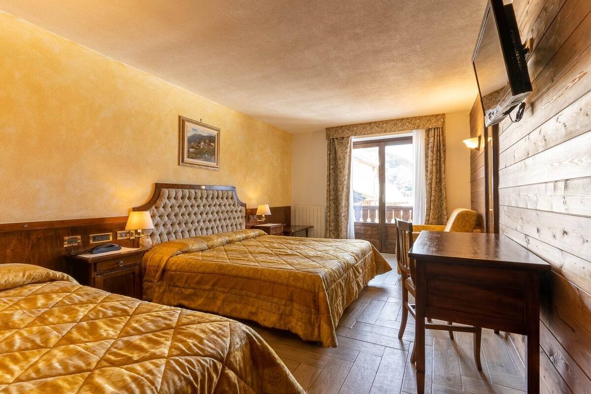 A hotel room with two beds, a desk, and a window with curtains.