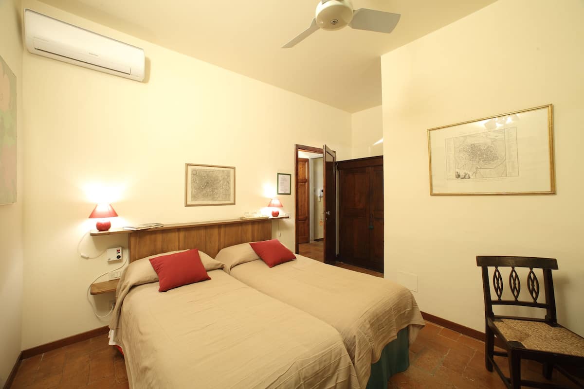A hotel room with two beds, a ceiling fan, an air conditioner, a framed map, and a wooden chair.