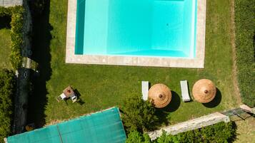 Vista aérea de una piscina rectangular rodeada por una terraza de piedra, con dos sillas de descanso y dos sombrillas de sol.