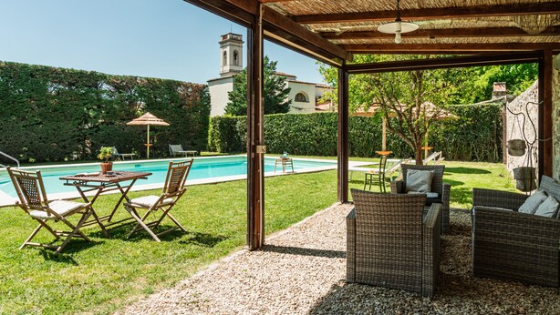 A covered outdoor area with a pool, wicker furniture, and a view of a church tower.