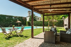 A covered outdoor area with a pool, wicker furniture, and a view of a church tower. - B&B Rovezzano (Florence)