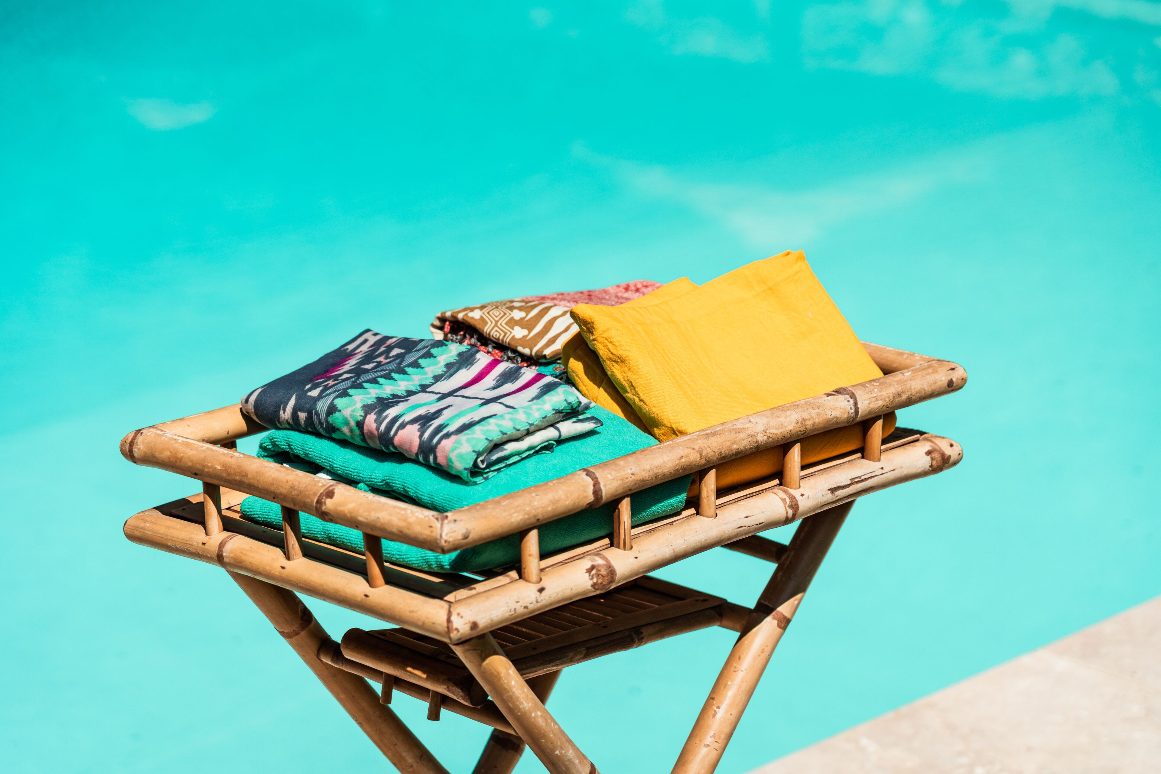 A bamboo lounge chair with a cushion and a yellow pillow by a pool.