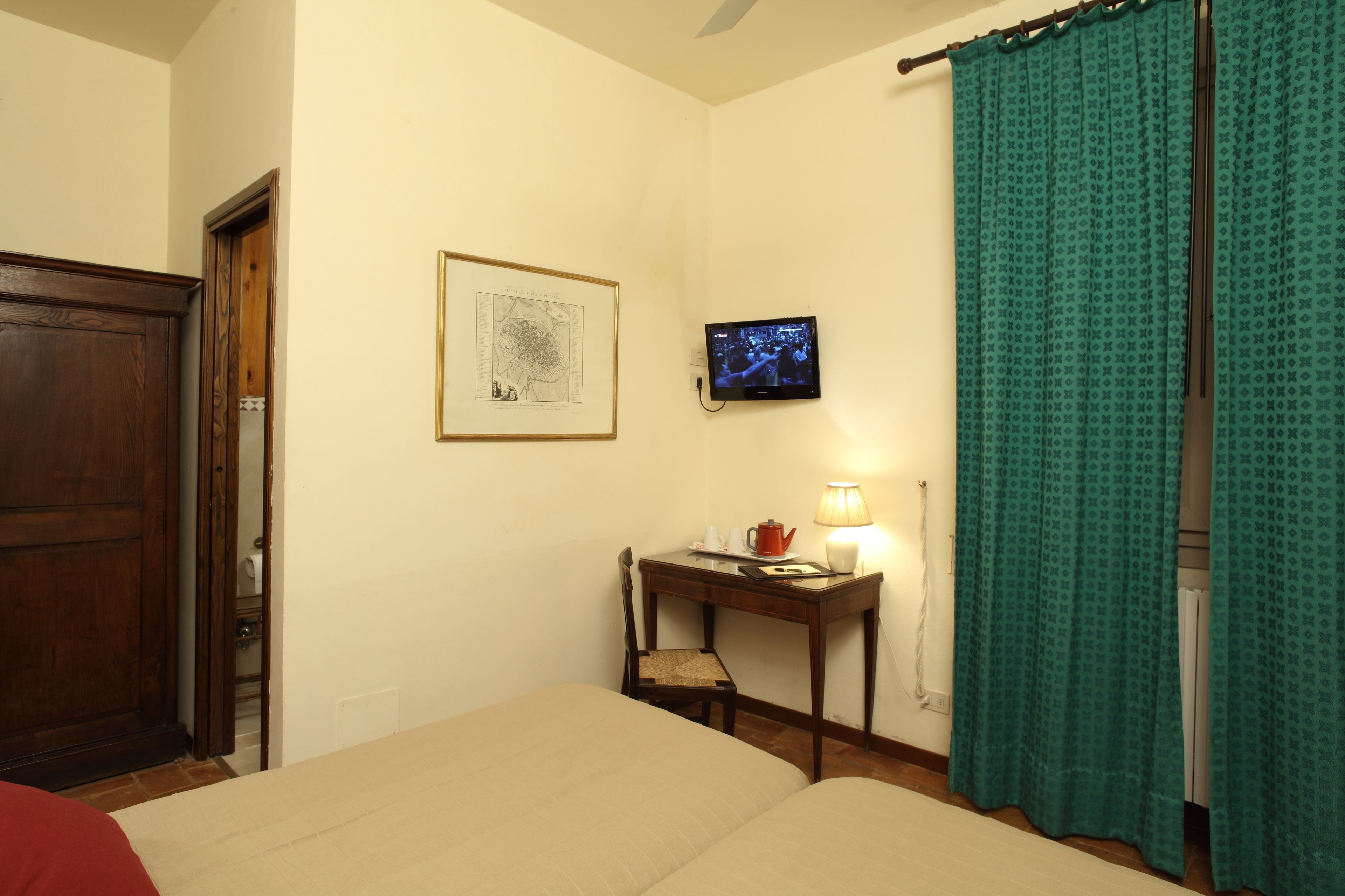 A hotel room with a bed, a desk with a chair, a television, and a framed map on the wall.