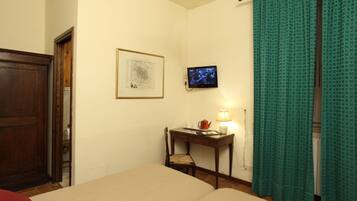 A hotel room with a bed, a desk with a chair, a television, and a framed map on the wall.