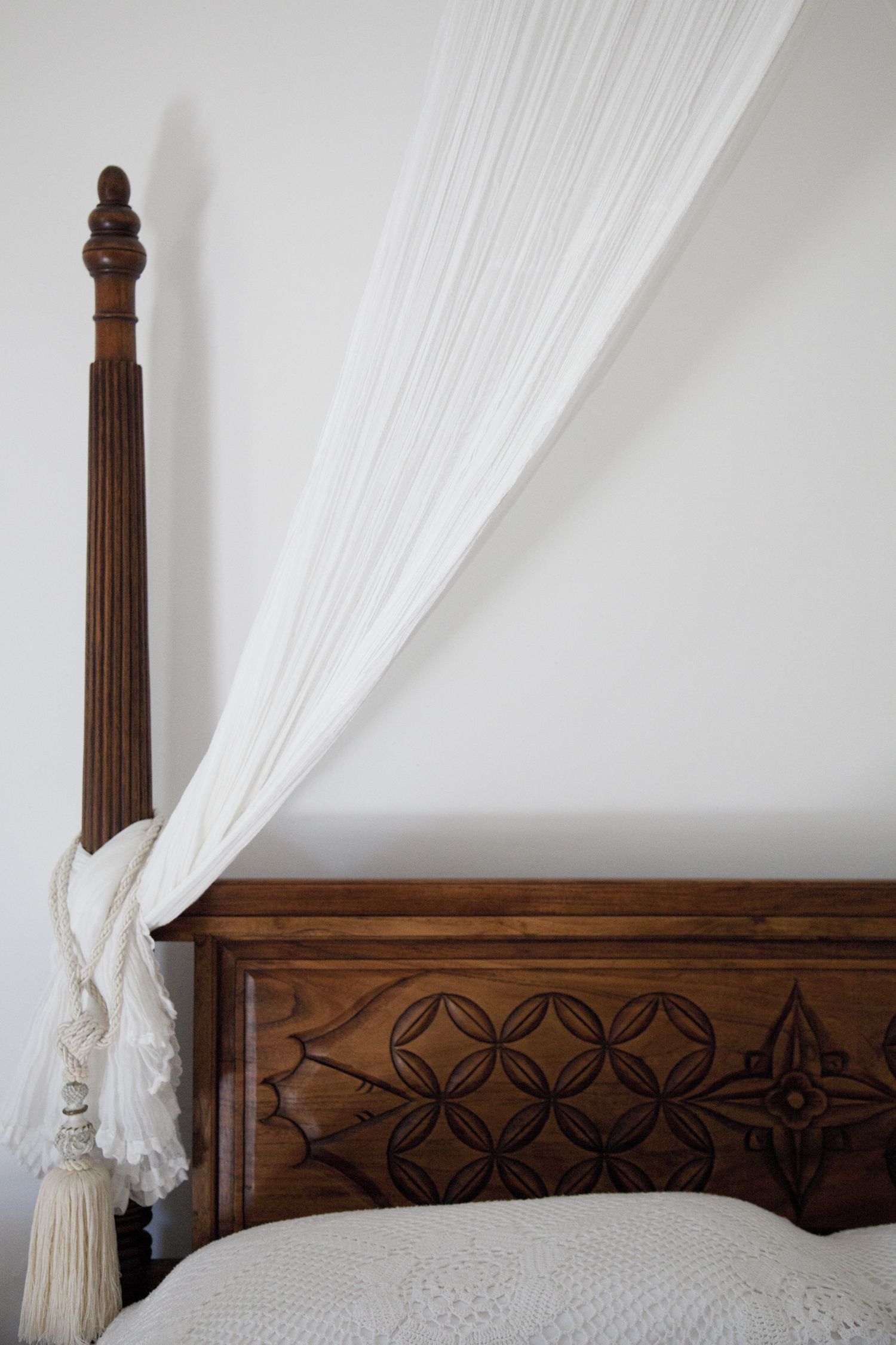 A bed with a wooden headboard featuring a geometric pattern, a white canopy, and a decorative tassel.