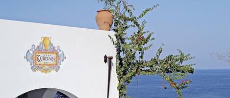 A hotel named "Quartara" with a large terracotta pot on the roof, a decorative emblem, and a view of the sea.