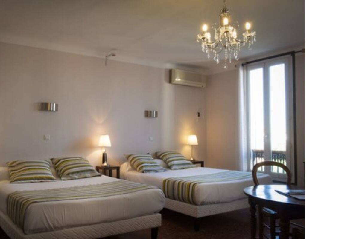 A hotel room with two beds, a chandelier, a dining table, and a window.