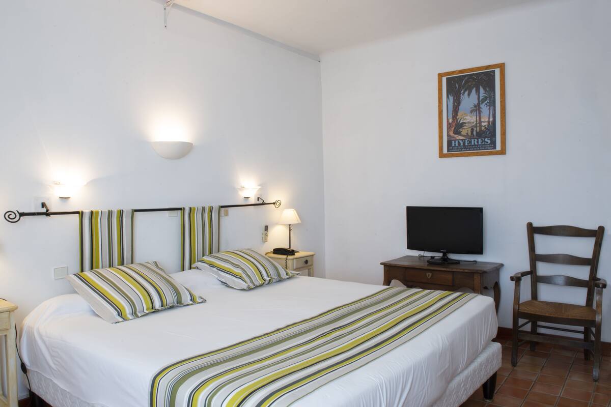 A neatly arranged bedroom with a bed, bedside lamps, a television, and a chair.