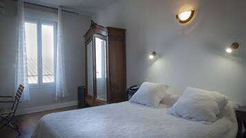 Ein Schlafzimmer mit einem großen Bett, einem Holzschrank, einem Sessel und einem Fenster mit Vorhängen.