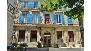 Un edificio histórico con una entrada central, varias ventanas con contraventanas azules y banderas.