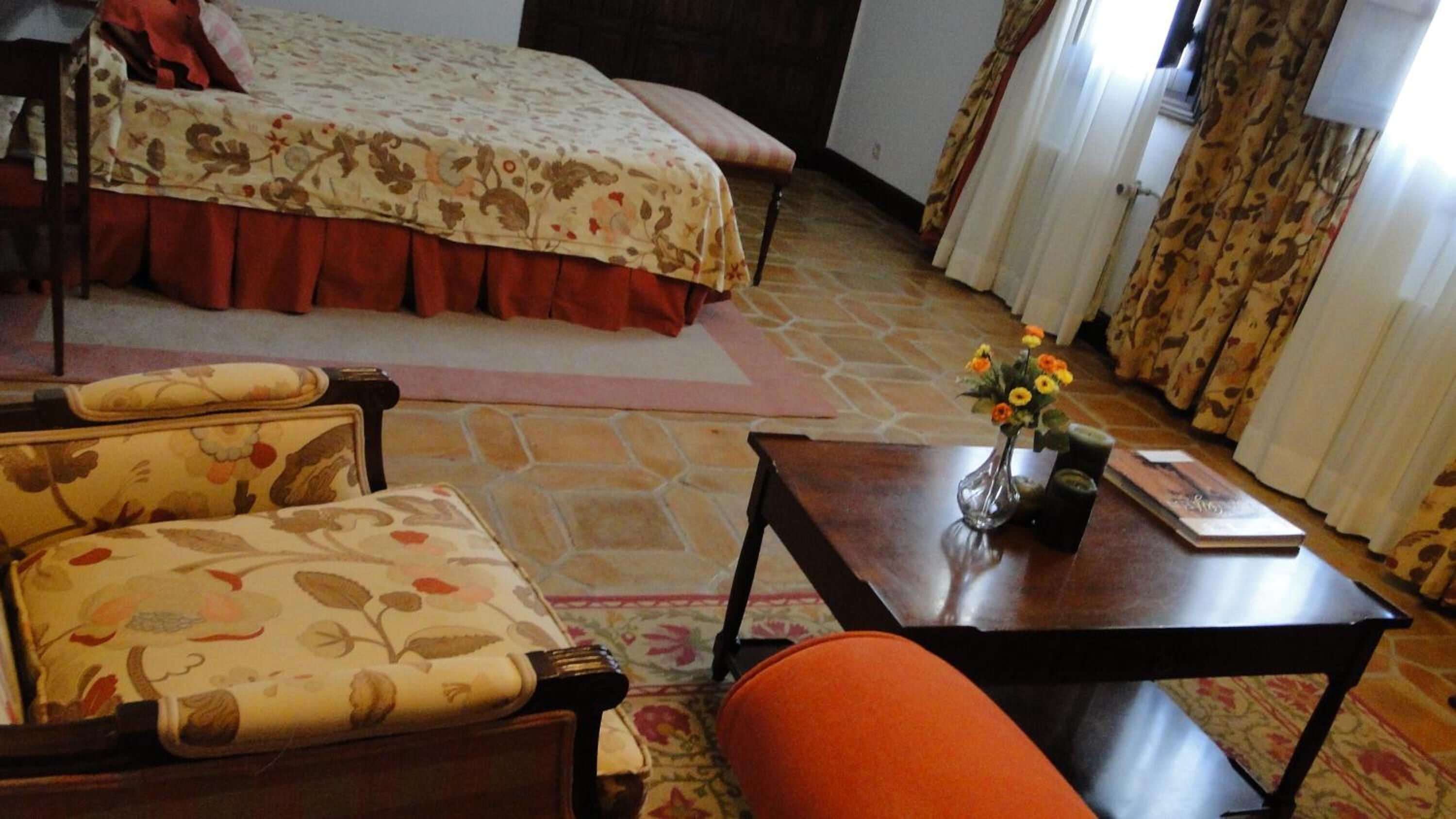 A bedroom with a bed, a chair, a table, and a vase with flowers.