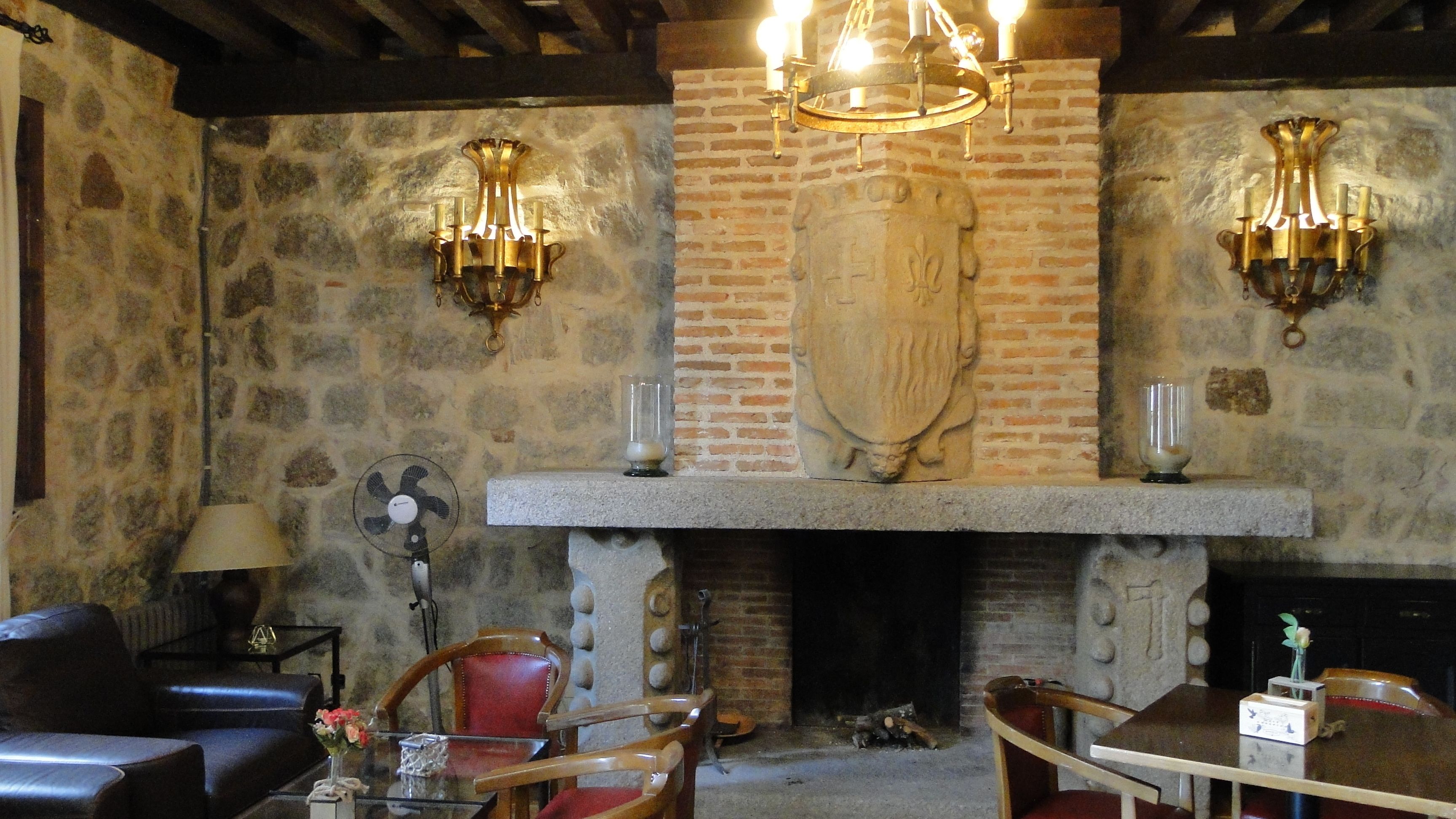 Una habitación de paredes de piedra con chimenea, dos candelabros fijos a la pared, asientos de cuero y una mesa de madera.
