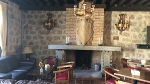 A cozy room with a stone fireplace, wooden furniture, and a chandelier. - Hotel Vettonia (Ávila)