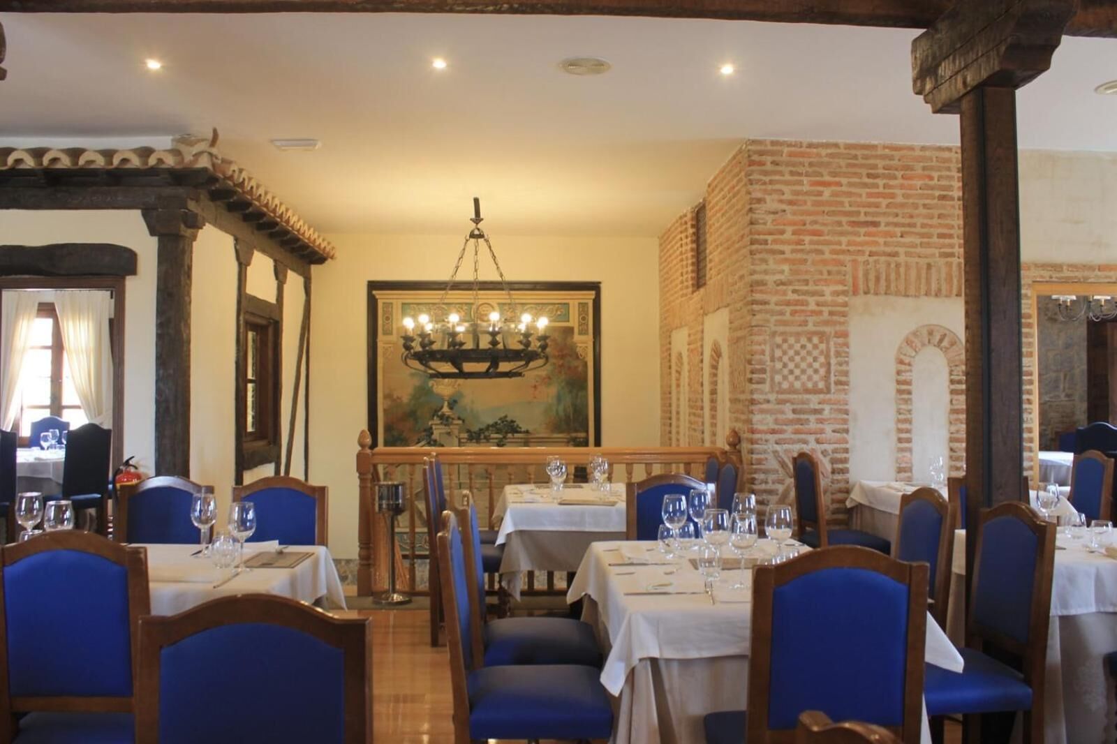 Un restaurant avec plusieurs tables et des chaises bleues, un lustre et un mur en briques.