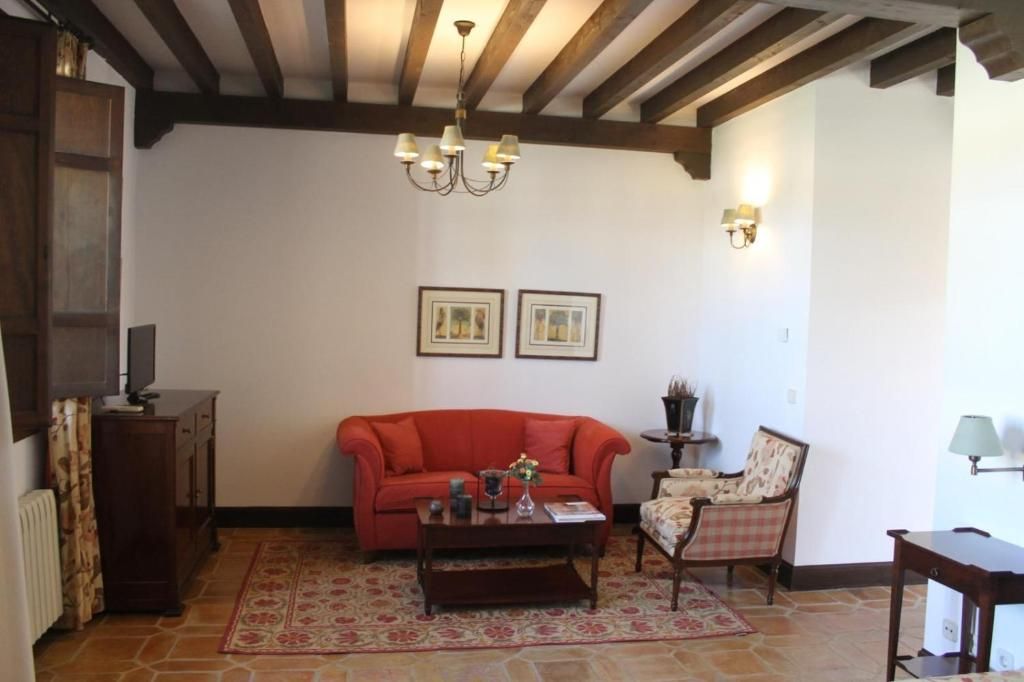 Una sala de estar con un sofá rojo, una mesa de centro de madera, una alfombra estampada, una silla, un televisor y cuadros enmarcados en la pared.