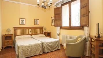 A double bed with a wooden headboard, two bedside tables, a chair, a radiator, and a window with curtains.