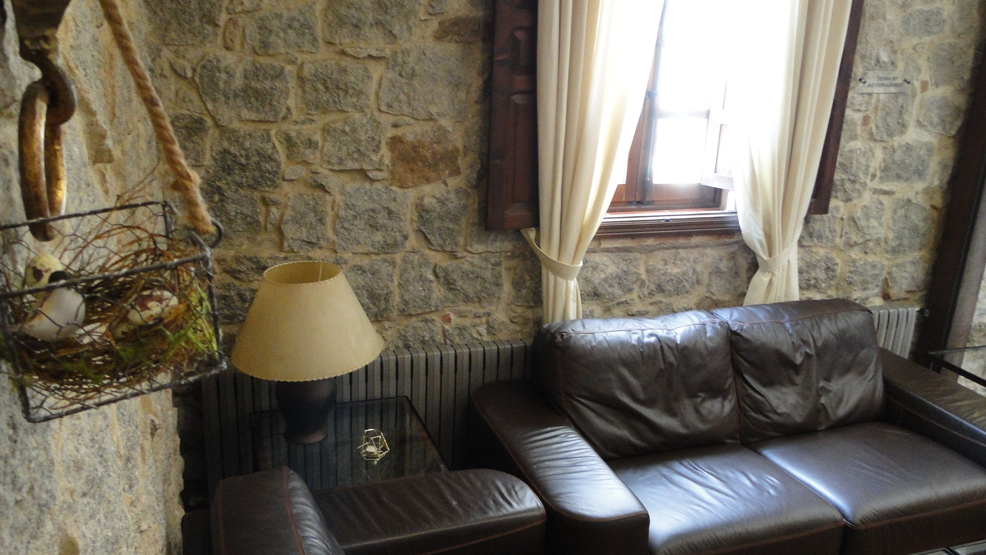 A stone-walled room with a leather sofa, a lamp, and a window with curtains.