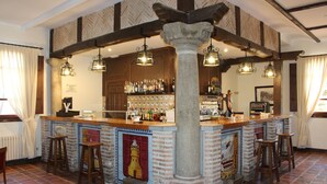 A bar area with a stone column, wooden beams, hanging lights, and a tiled backsplash. - Hotel Vettonia (Ávila)